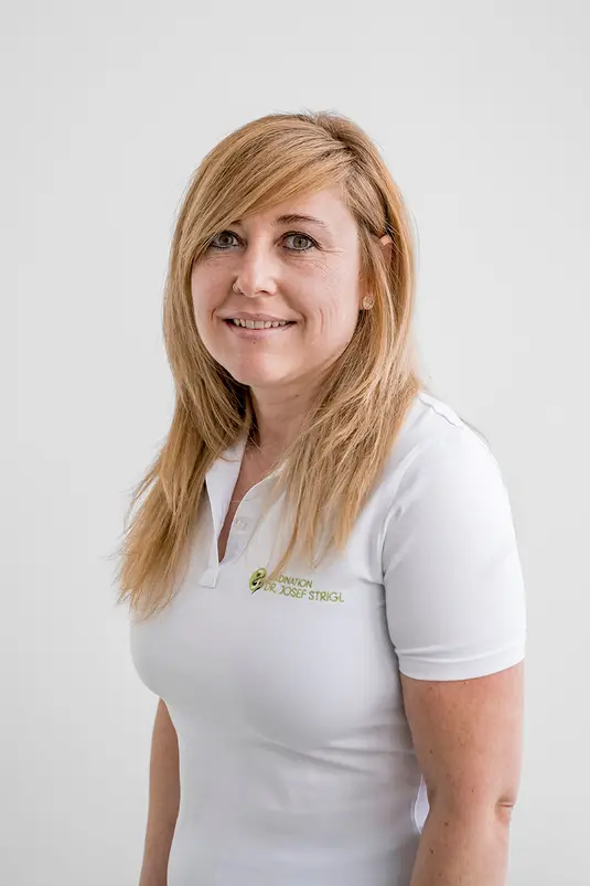 Frau mit langen blonden Haaren und weißem Polohemd vor einem schlichten weißen Hintergrund, leicht lächelnd.